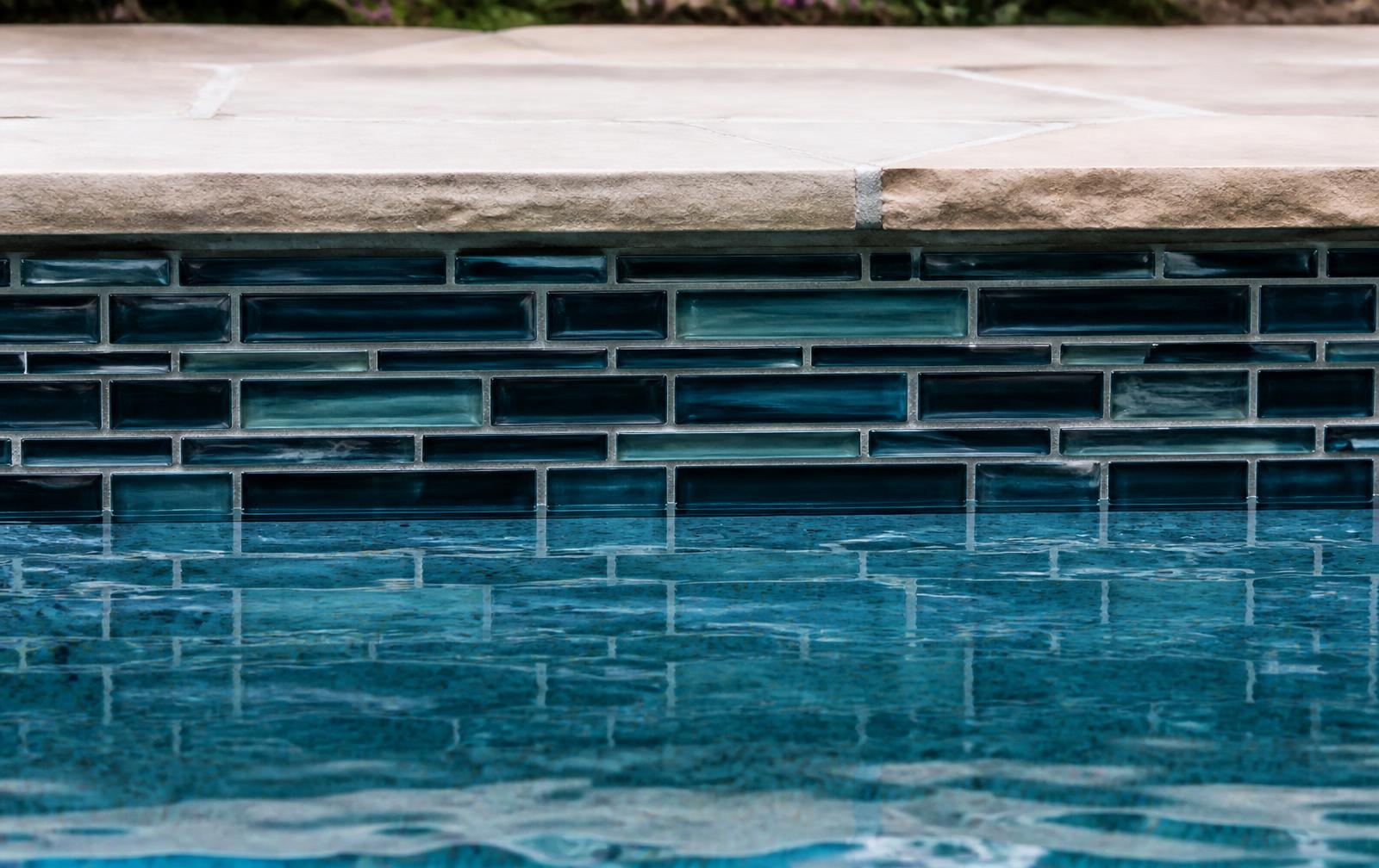 Restored pool waterline with clean glass mosaic tile and stone coping