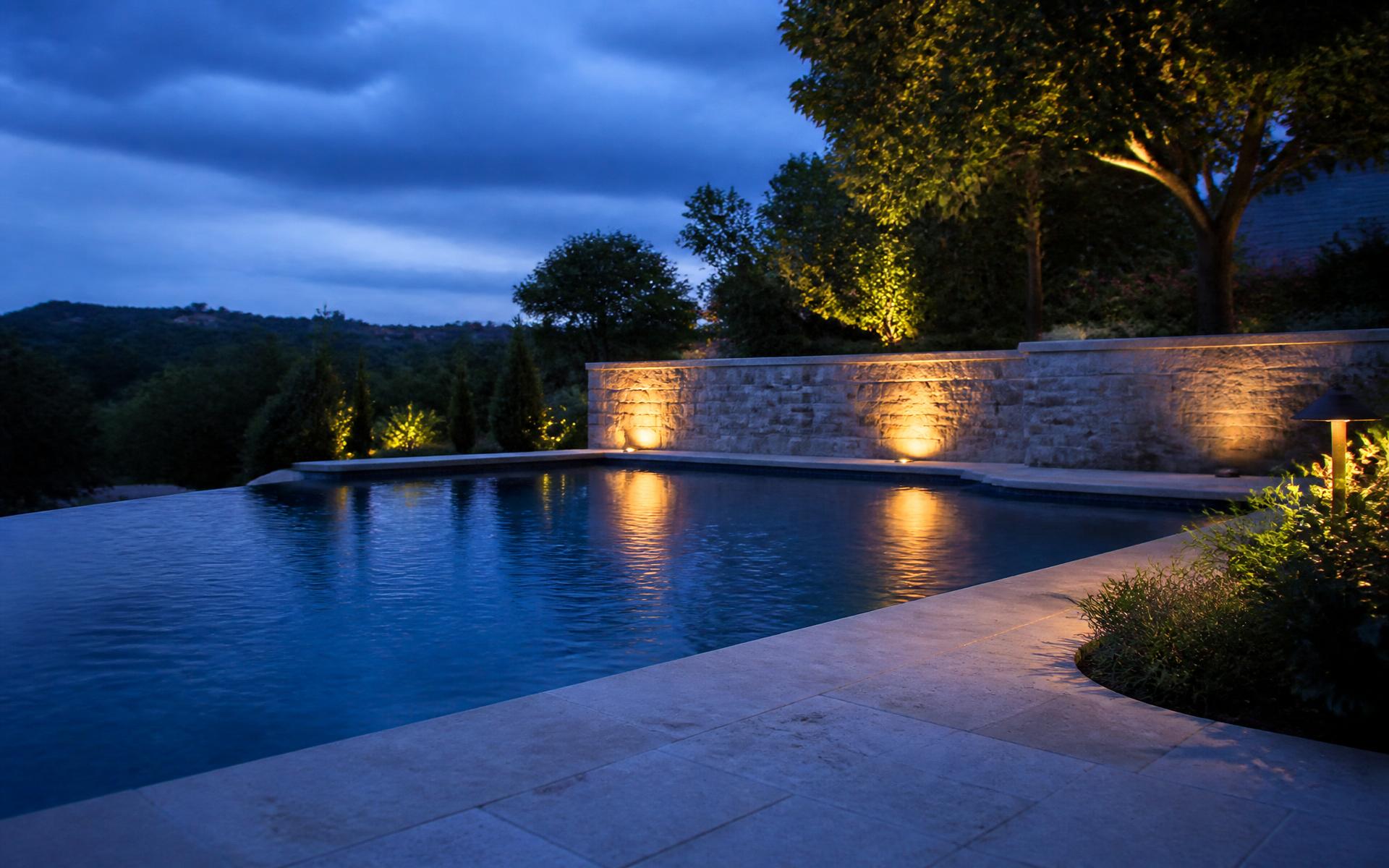 Residential pool at dusk with warm landscape lighting on a stone wall
